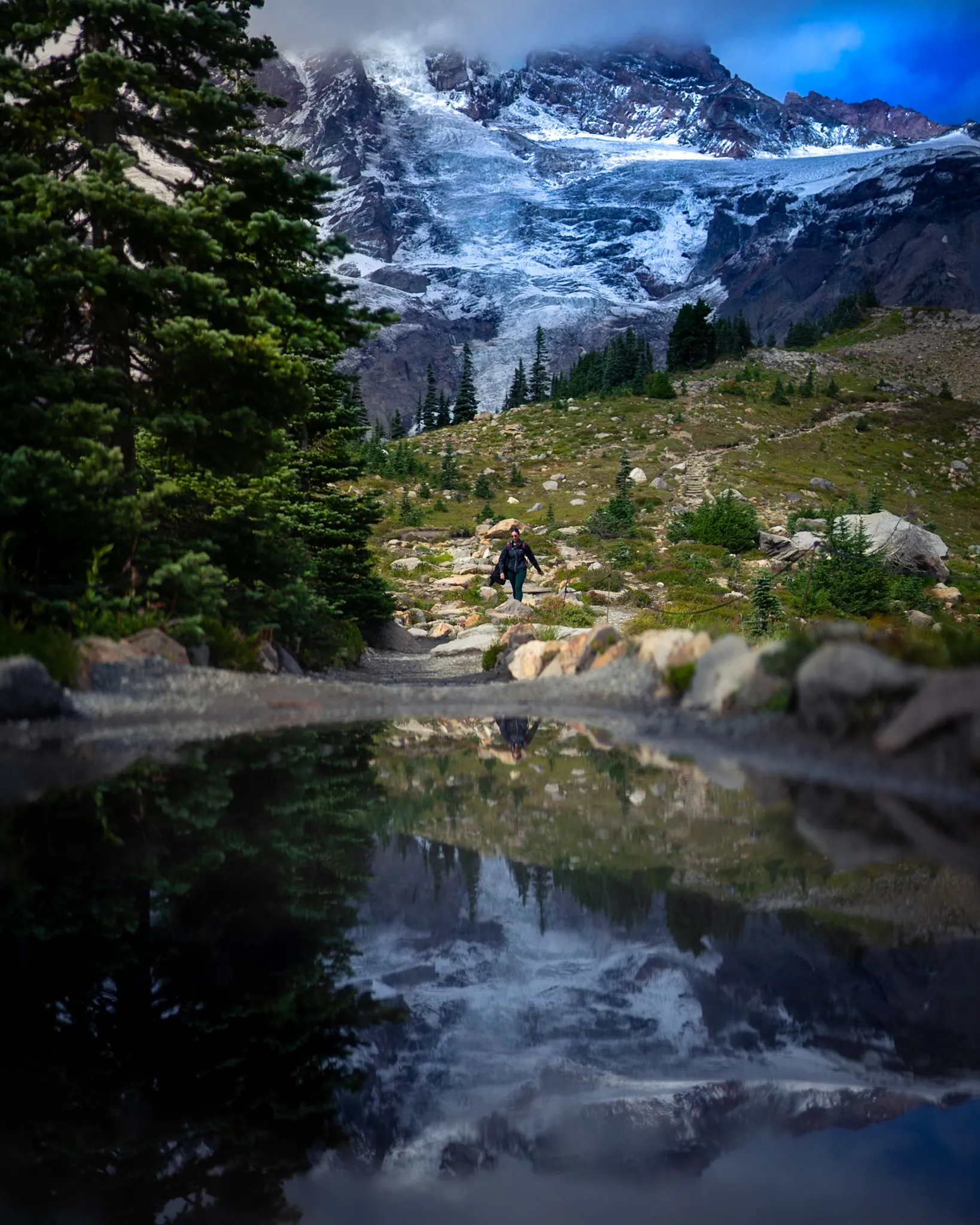 A hiker beside an alpine lake and snowy mountains
